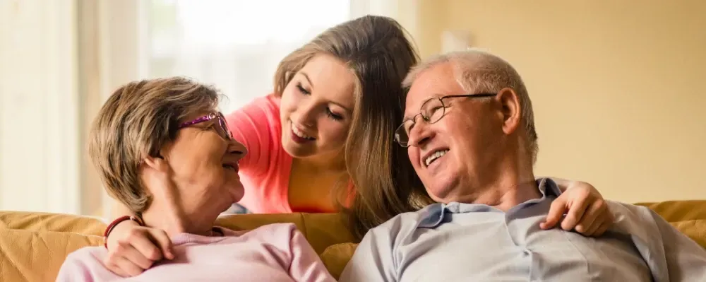 Two women and a man smiling and chatting on a couch in a warm living room