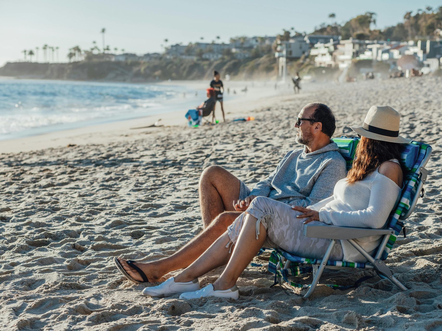 Couple relaxing in beach chairs on a sandy beach, enjoying the ocean view under a sunny sky.