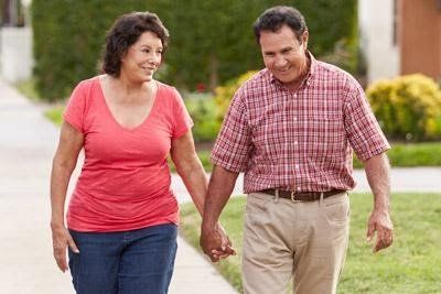 A man and a woman are walking down a sidewalk holding hands.