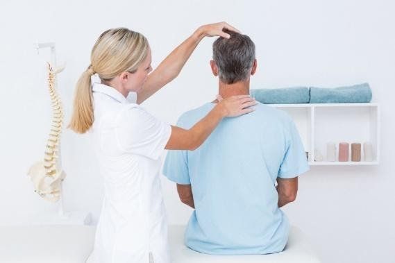 A woman is examining a man 's neck while he sits on a table.
