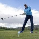 A man is swinging a golf club at a golf ball on a golf course.