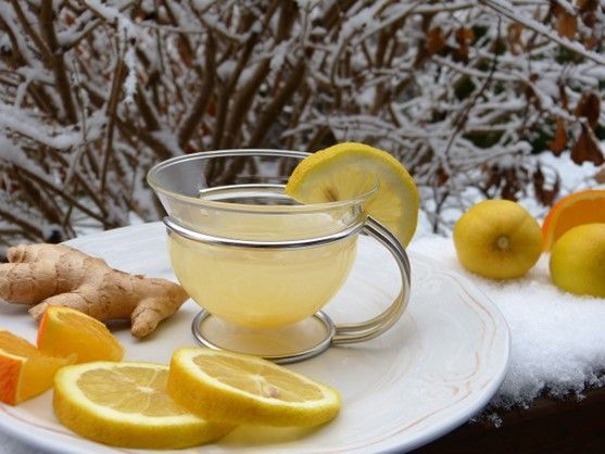 A cup of tea with lemon slices and ginger on a plate in the snow.
