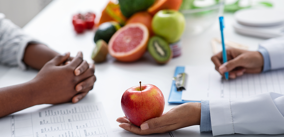 A woman is holding an apple in her hand while a doctor writes on a clipboard.