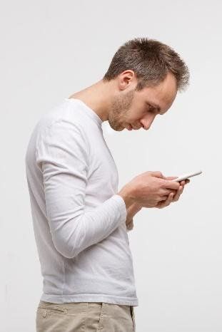 A man in a white shirt is looking at his cell phone.