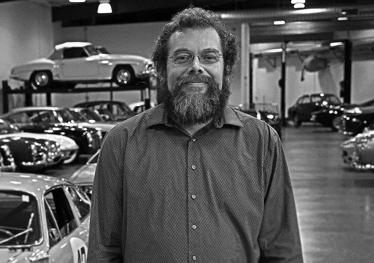 Bearded man standing in a car showroom with classic cars in the background. Bearded man standing in a car showroom with classic cars in the background.
