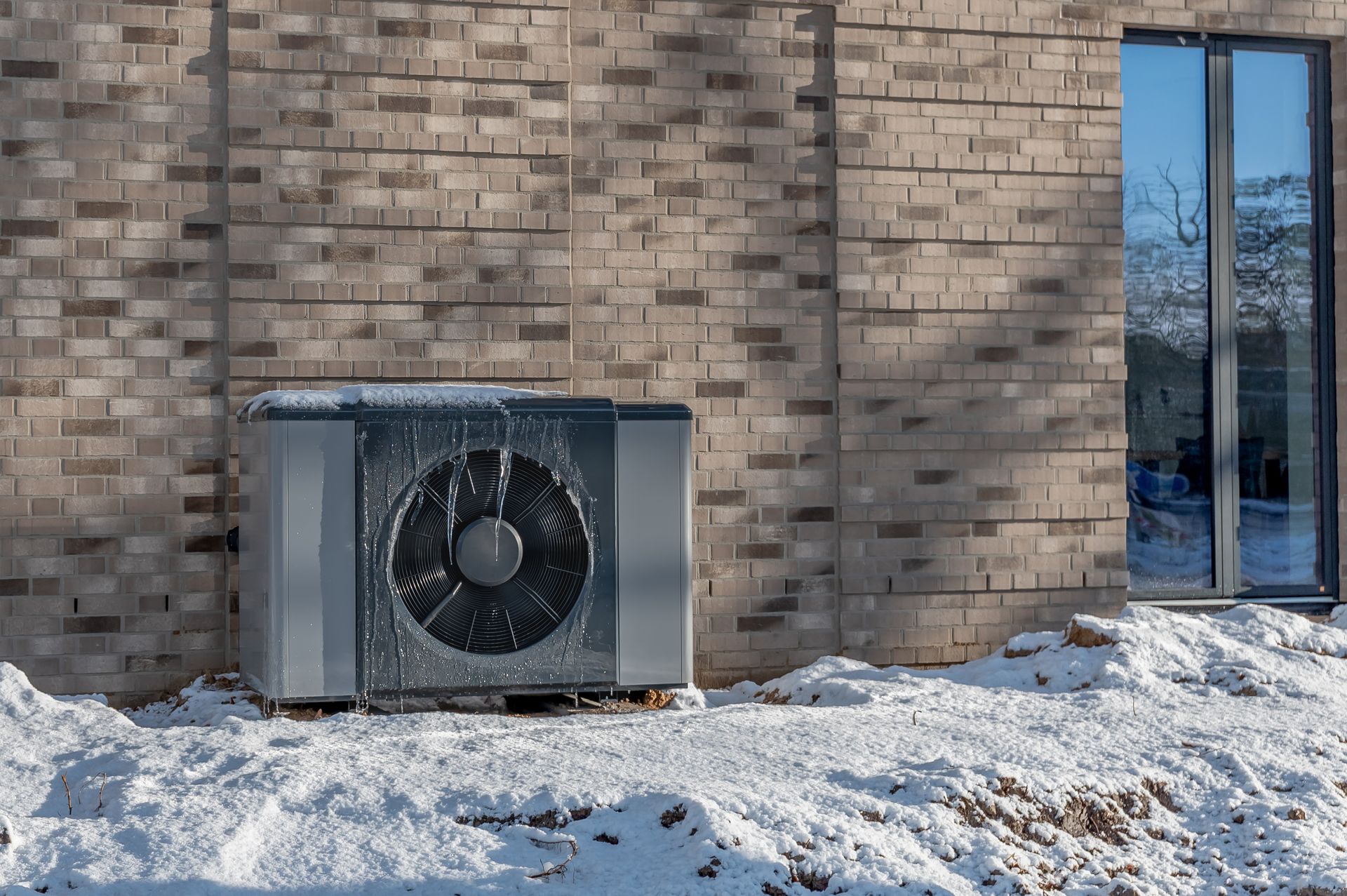 Frost-covered heat pump outdoor unit in snow that may need a heating repair contractor Frost-covered heat pump outdoor unit in snow that may need a heating repair contractor