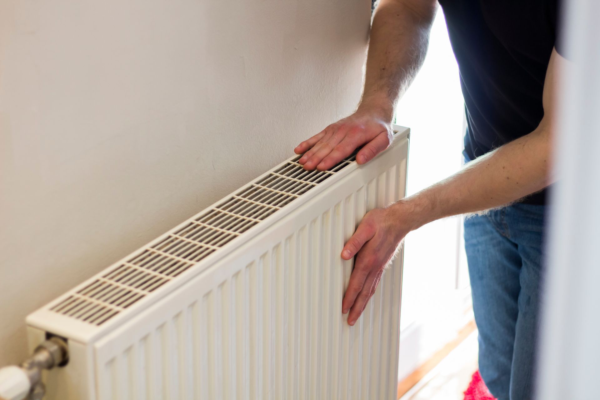 Person adjusting a white radiator in a bright room
