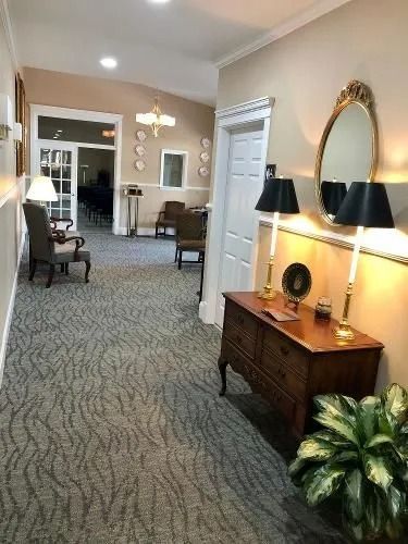 Hallway with beige walls, patterned carpet, antique furniture, and a potted plant.