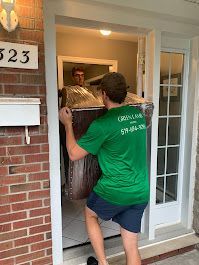 A man in a green shirt is carrying a large piece of furniture into a house.