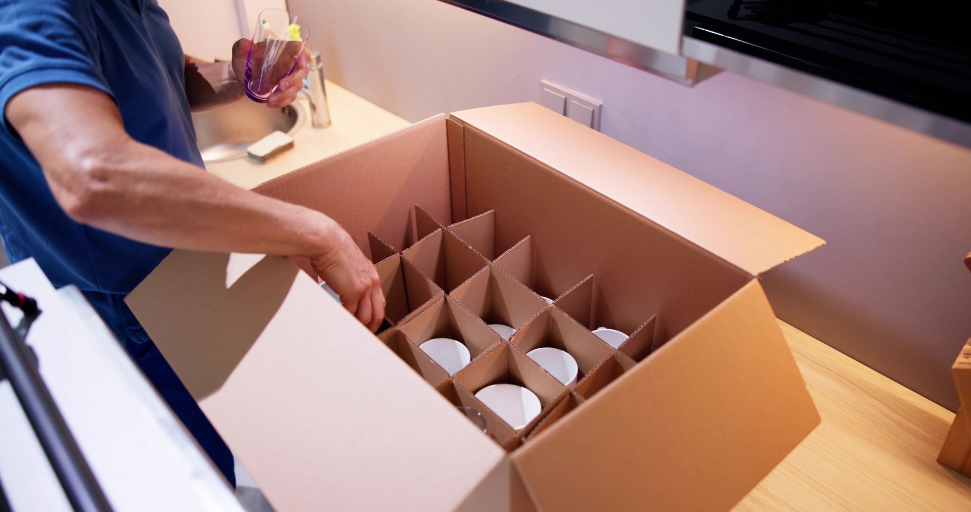 A man is packing a cardboard box with plates in it.
