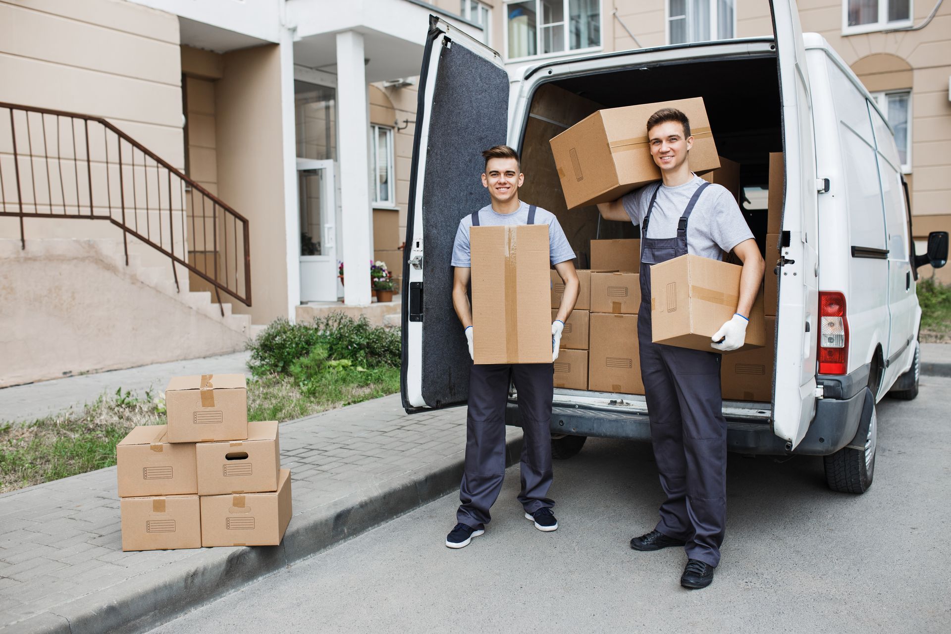 Two movers loading boxes into a van, in front of a building.