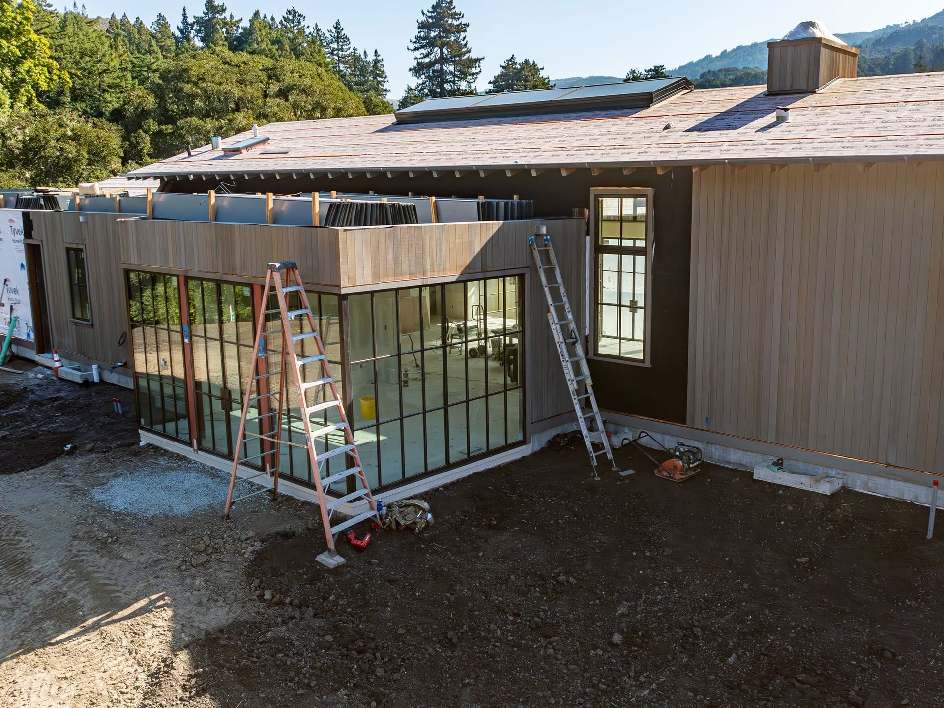 House under construction with ladders, glass panels, and a partially covered patio frame