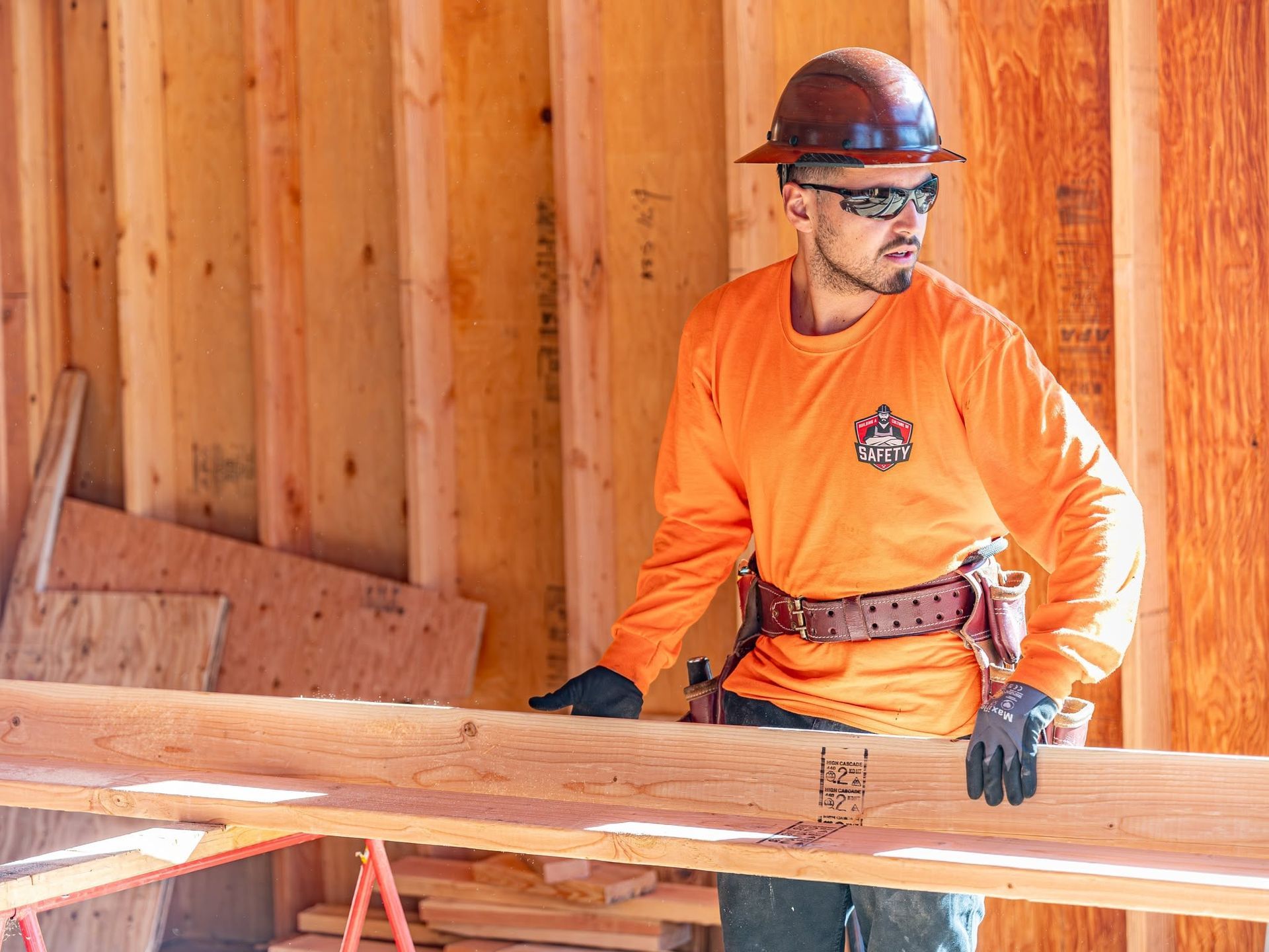 Construction worker in orange shirt guiding a wooden beam inside a framed building