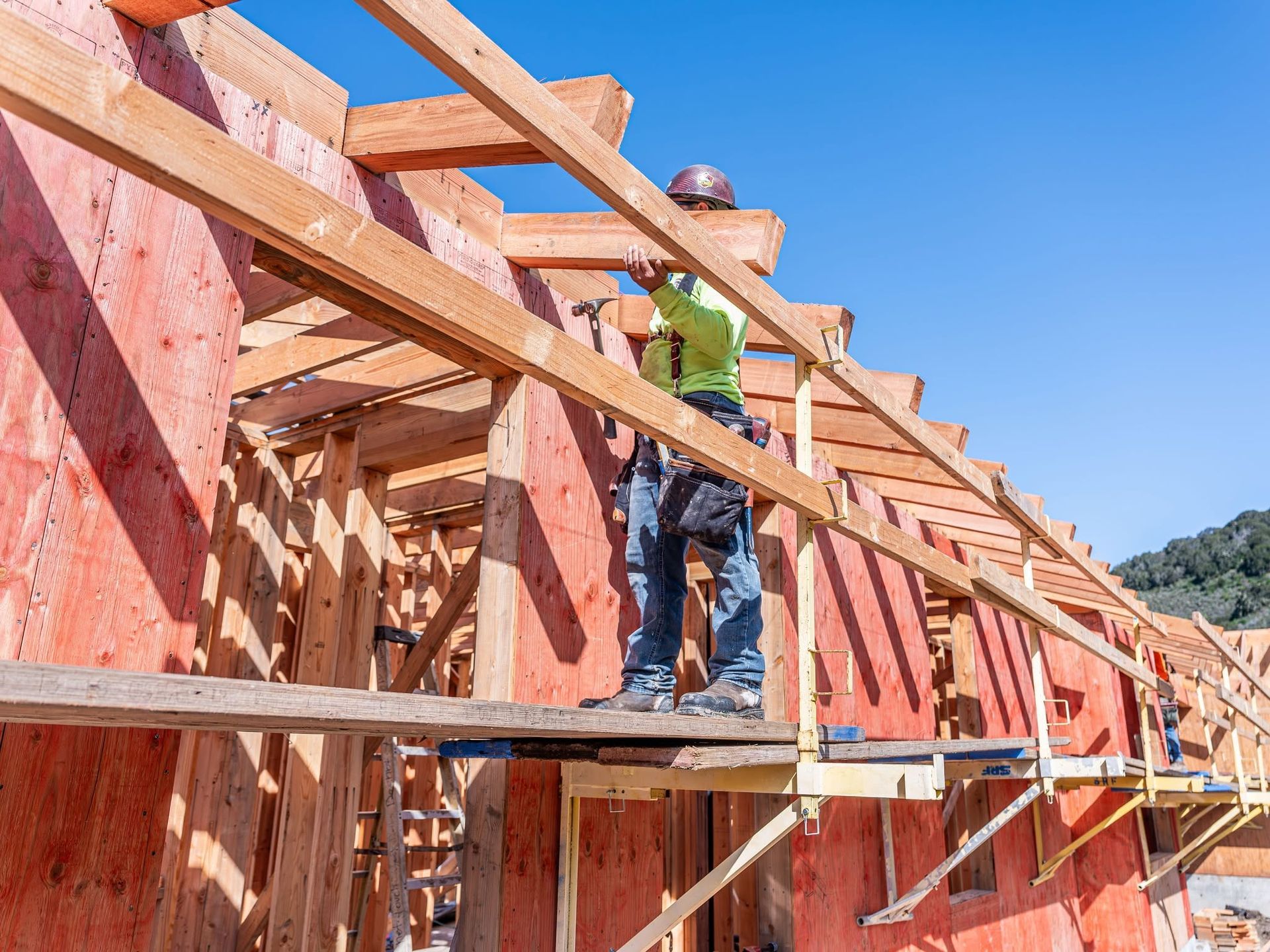 Worker on a wooden roof frame at a construction site under a clear blue sky