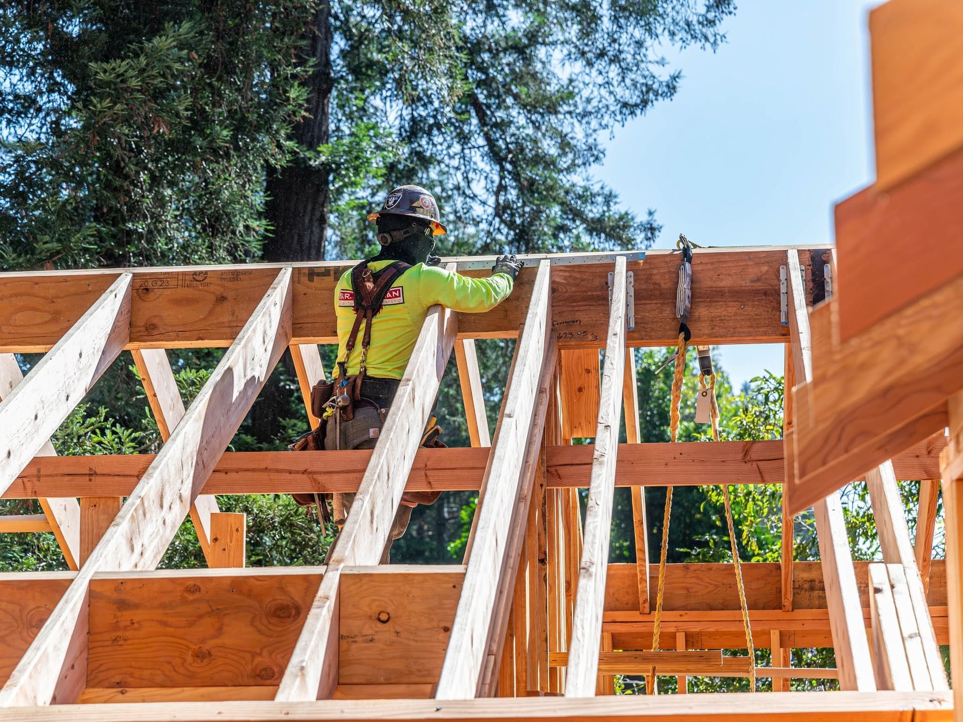 Construction worker framing a wooden house roof under a clear blue sky