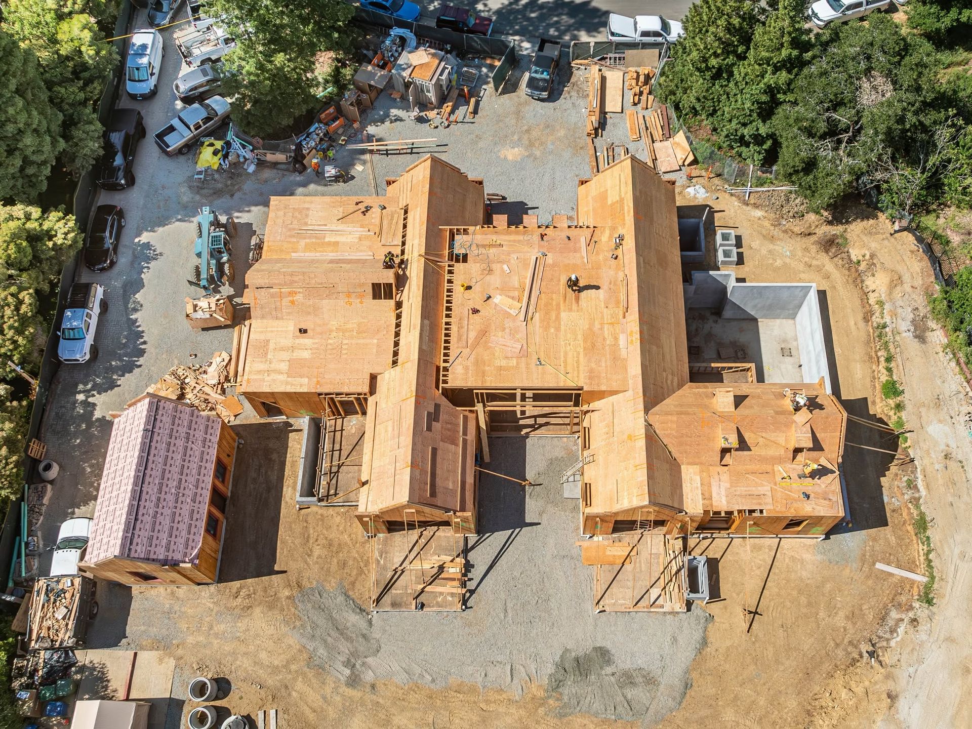 Aerial view of a house under construction with exposed wooden framing and surrounding worksite.