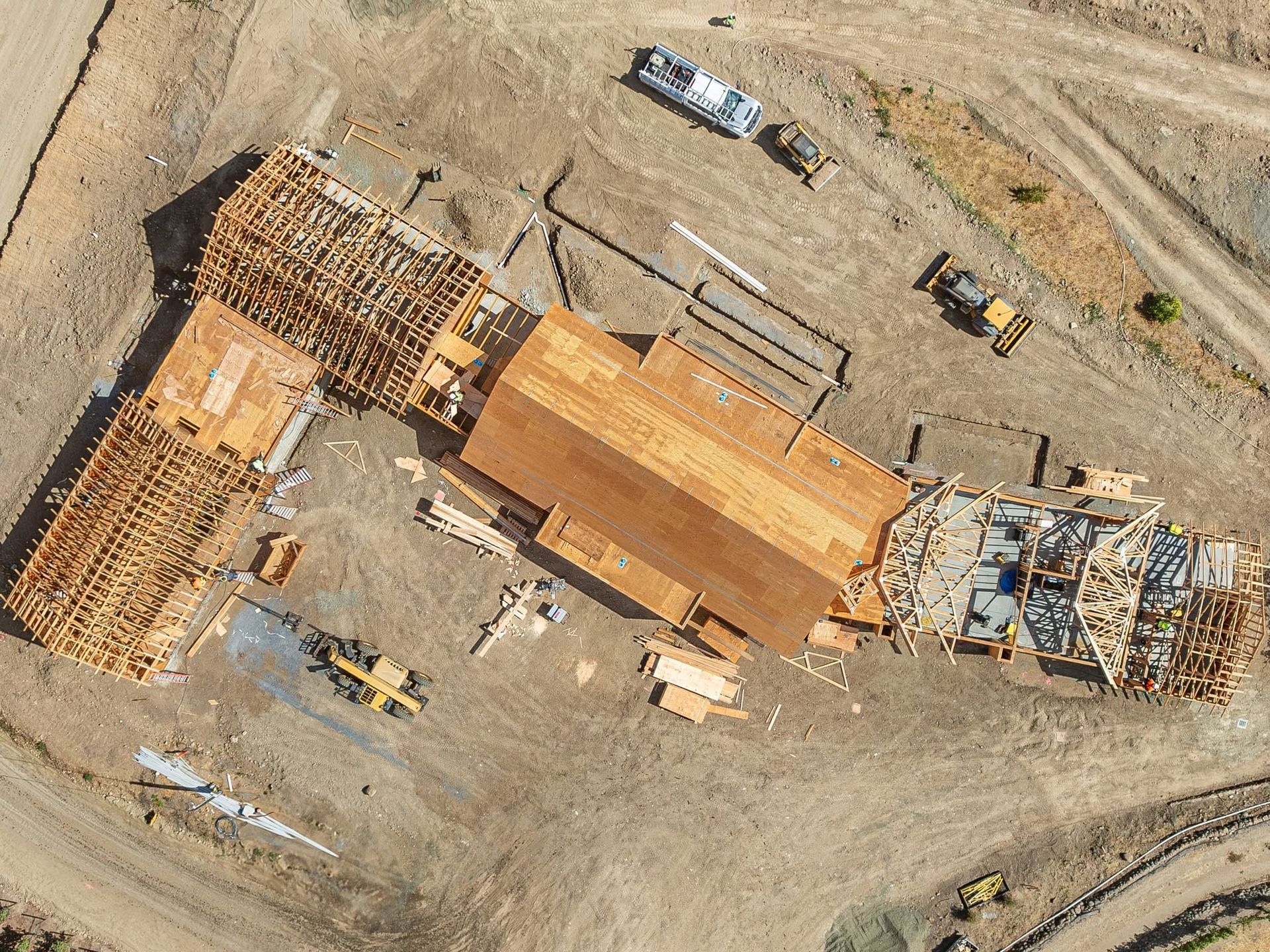 Aerial view of a large construction site with a long orange-roofed building and heavy equipment nearby