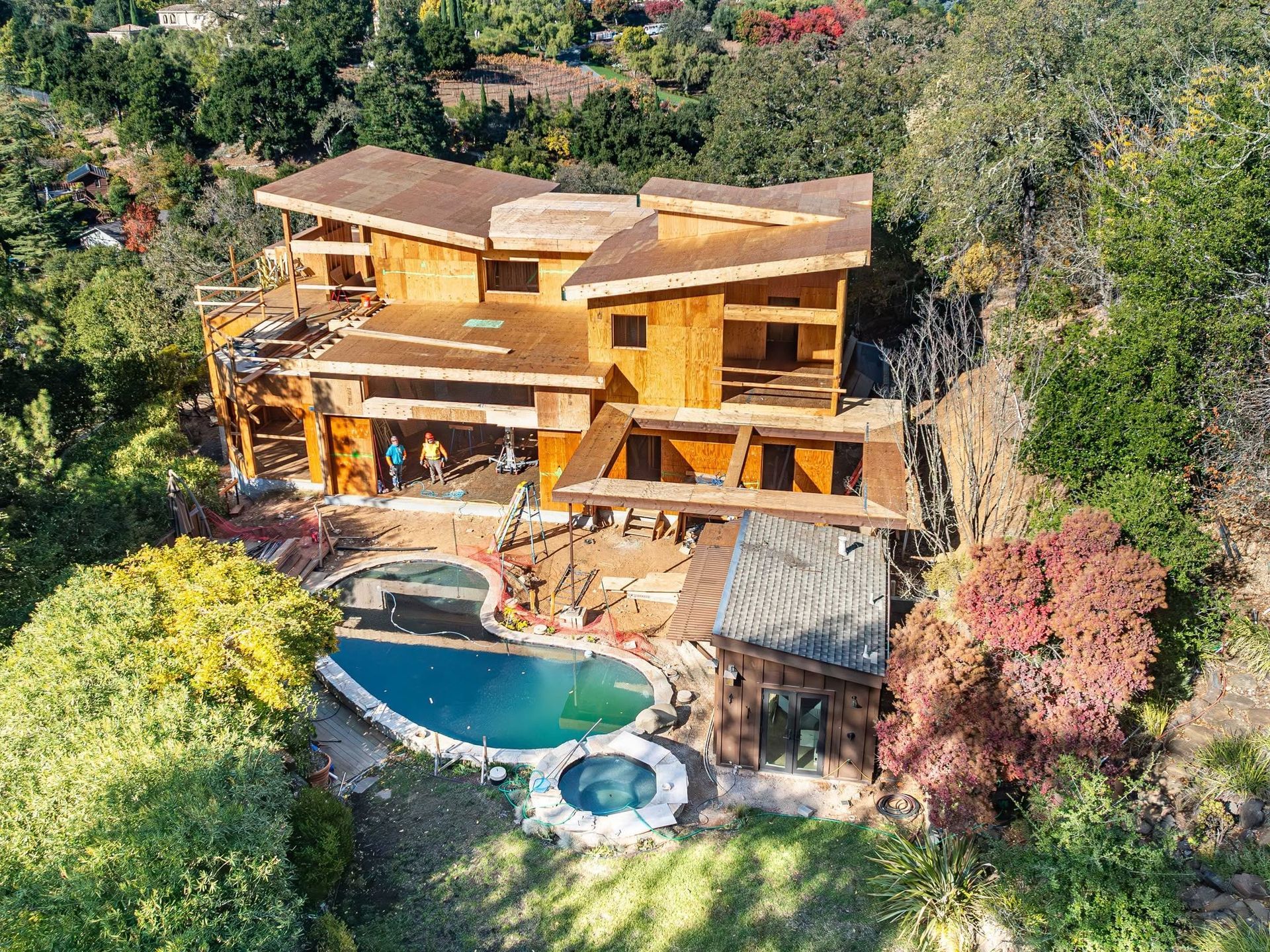 Wooden hillside house with a blue pool and hot tub surrounded by trees