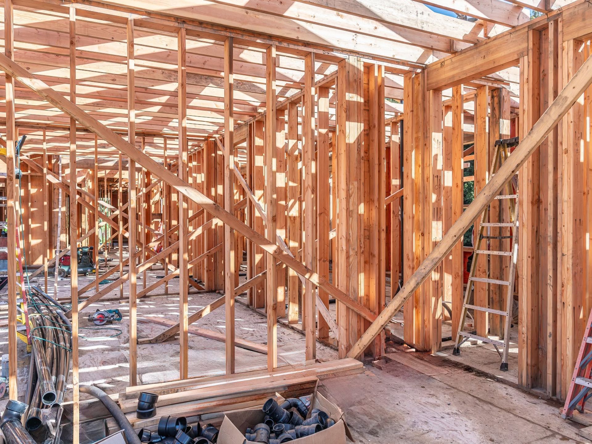 Wooden house framing under construction with exposed beams and scattered tools on the floor.