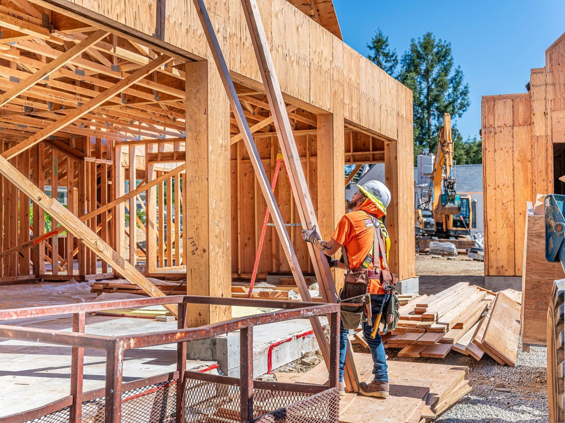 Construction worker on a wooden-framed building site, carrying tools beside lumber and scaffolding.