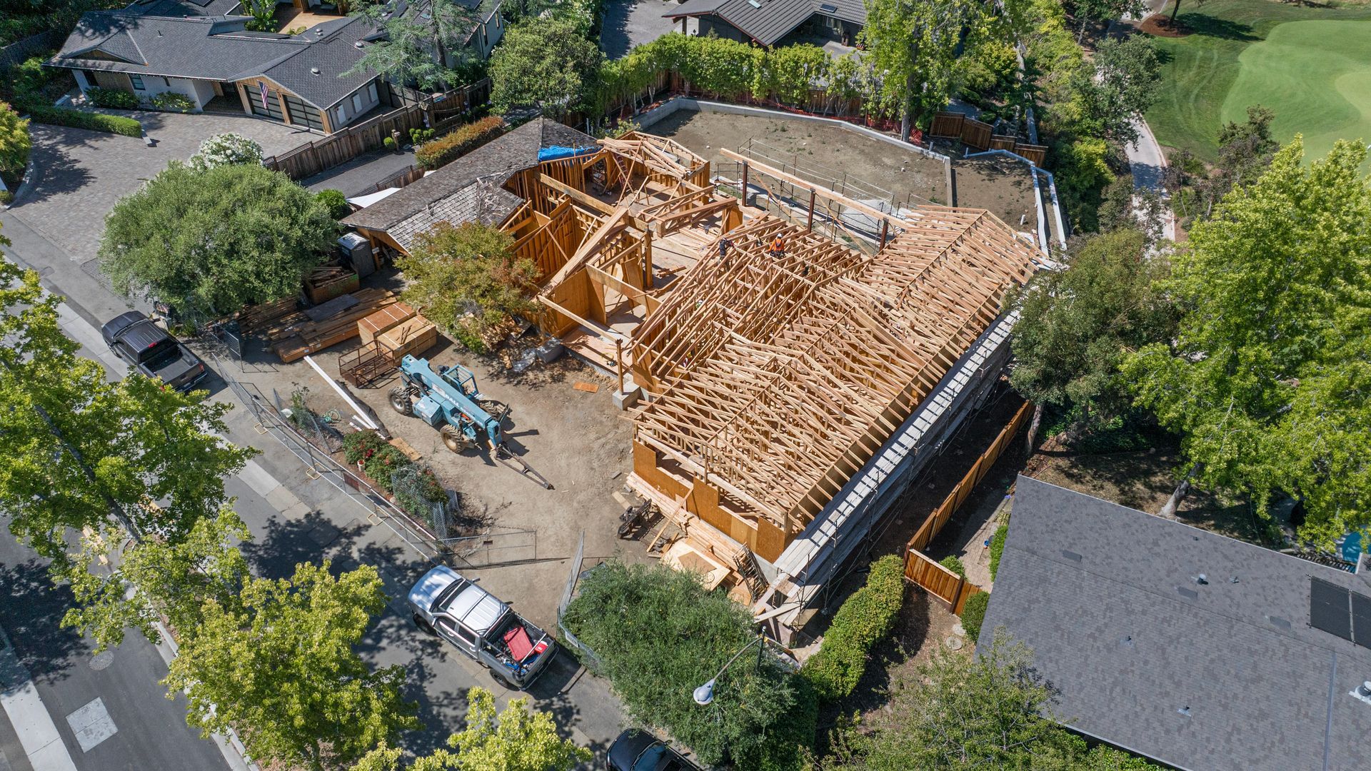 Aerial view of a house under construction with exposed wooden framing and nearby parked vehicles