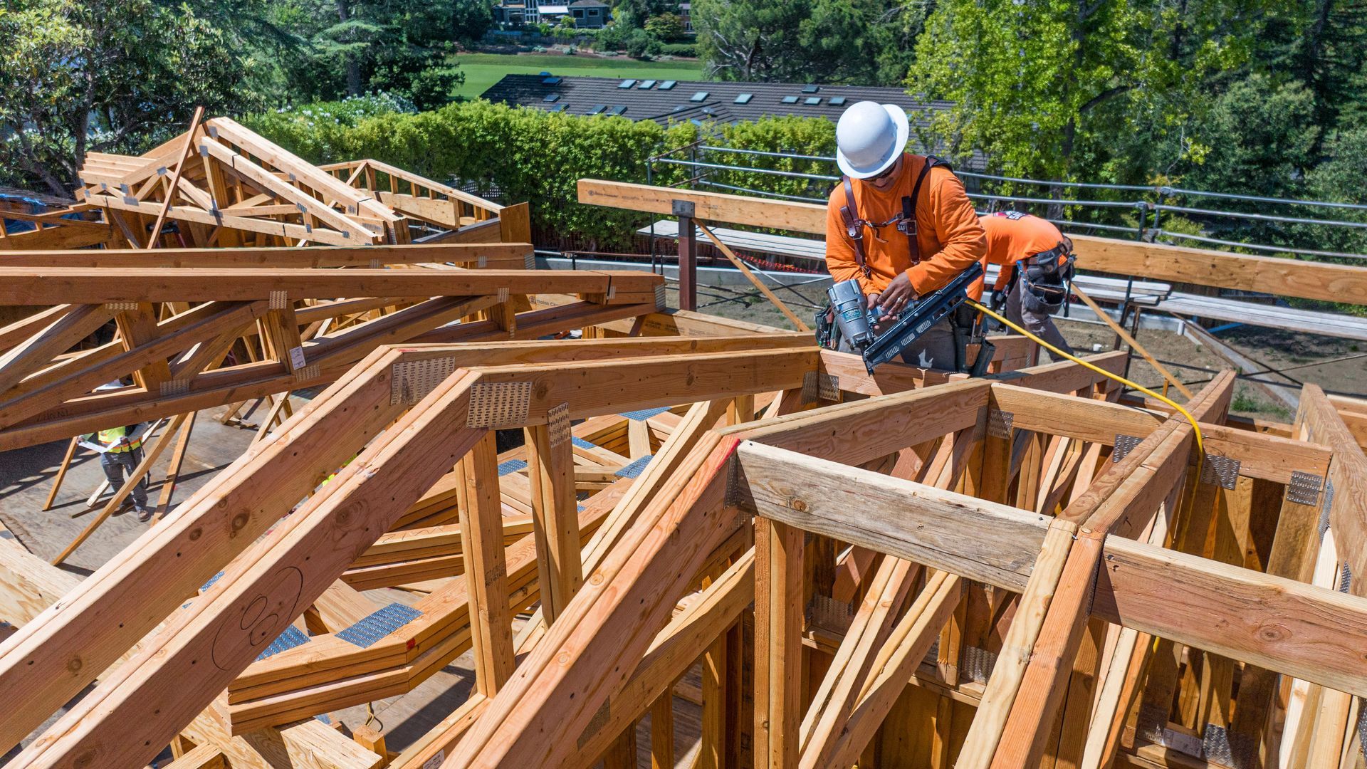 Construction worker in orange gear assembling wooden roof trusses at a building site