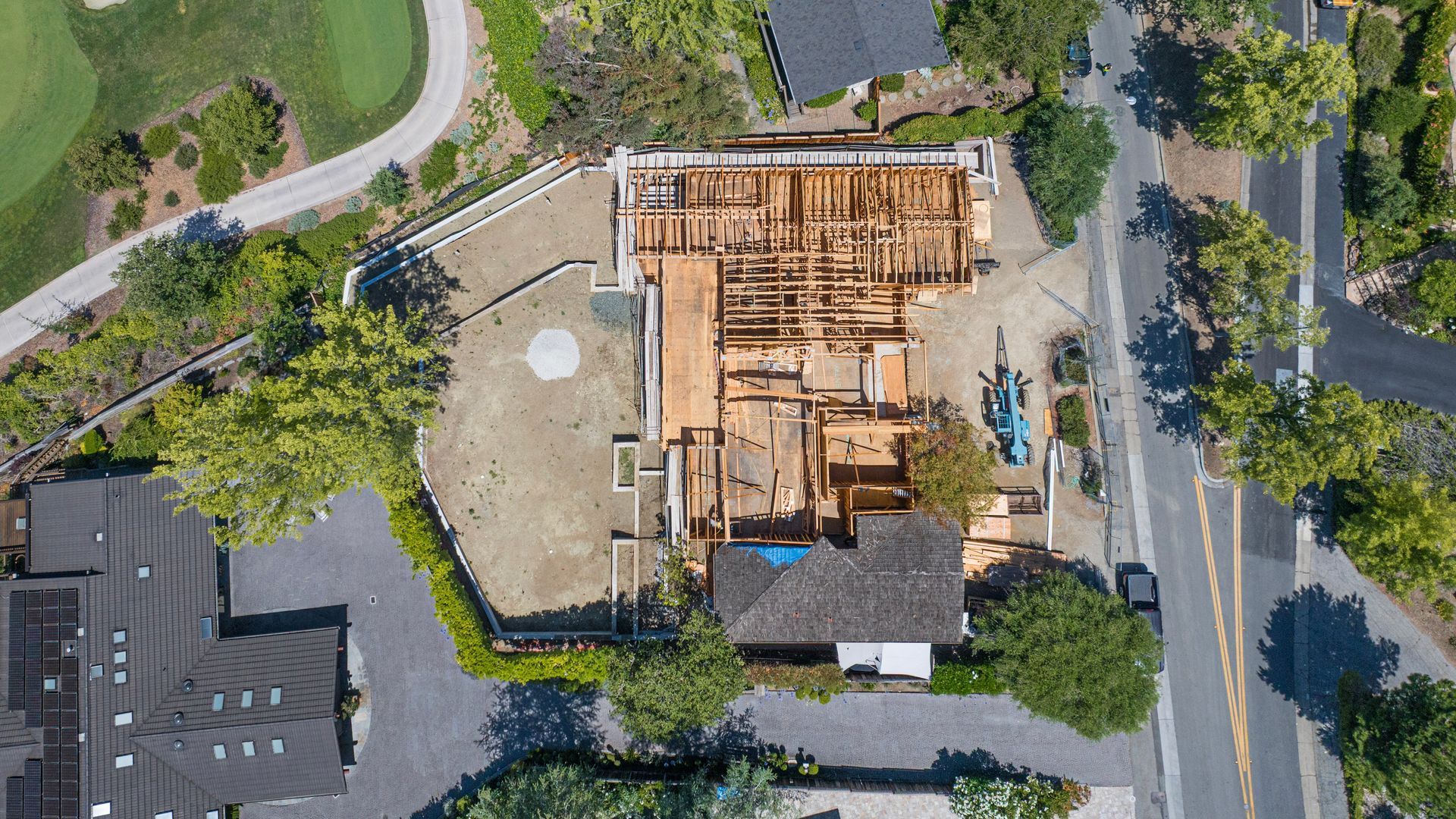 Aerial view of a house under construction with framing exposed, surrounded by trees and roads.