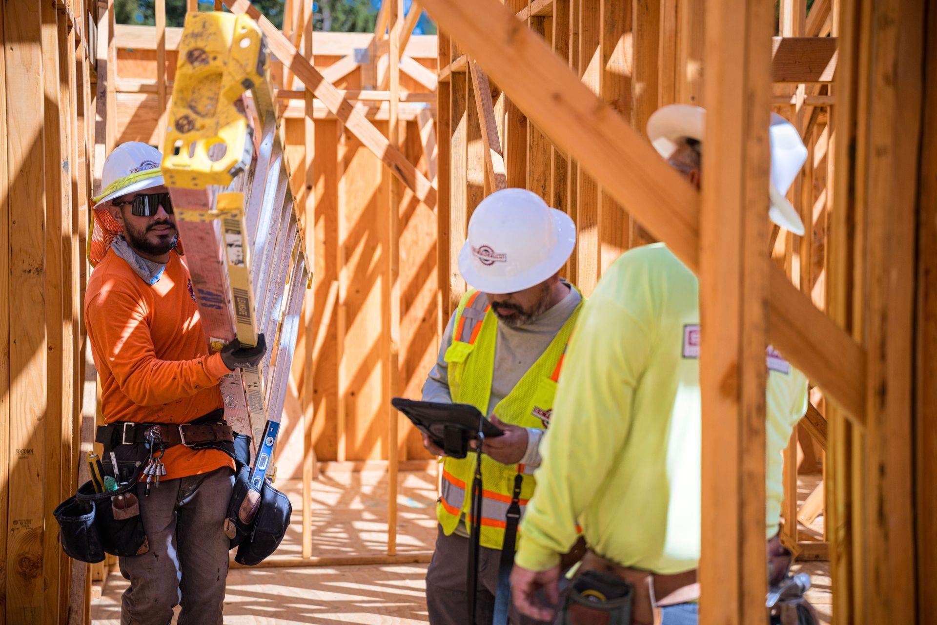 Construction workers in hard hats inspect wooden framing at a building site.