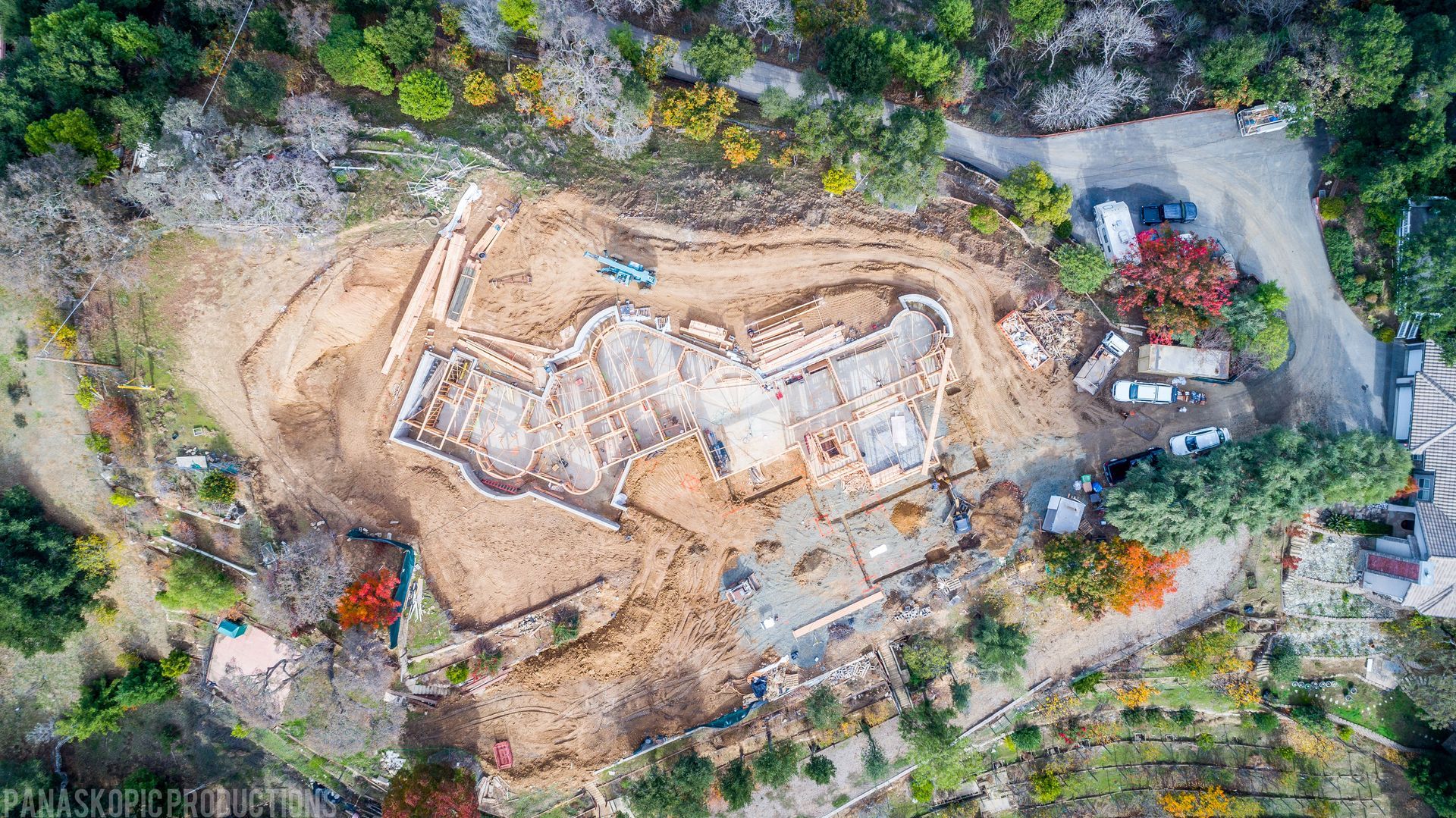 Aerial view of a construction site with a concrete foundation, dirt excavation, and surrounding trees.
