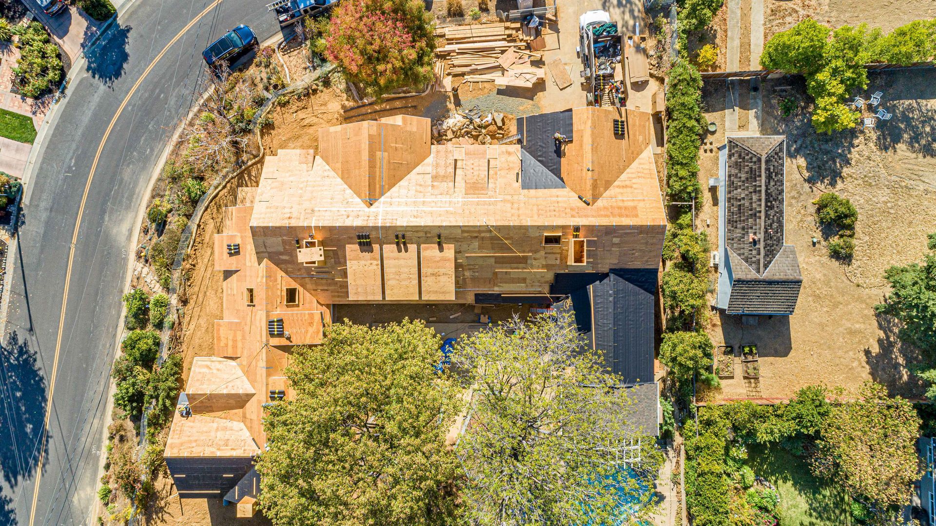 Aerial view of a tan-roofed house with trees, a driveway, and a small outbuilding beside it.