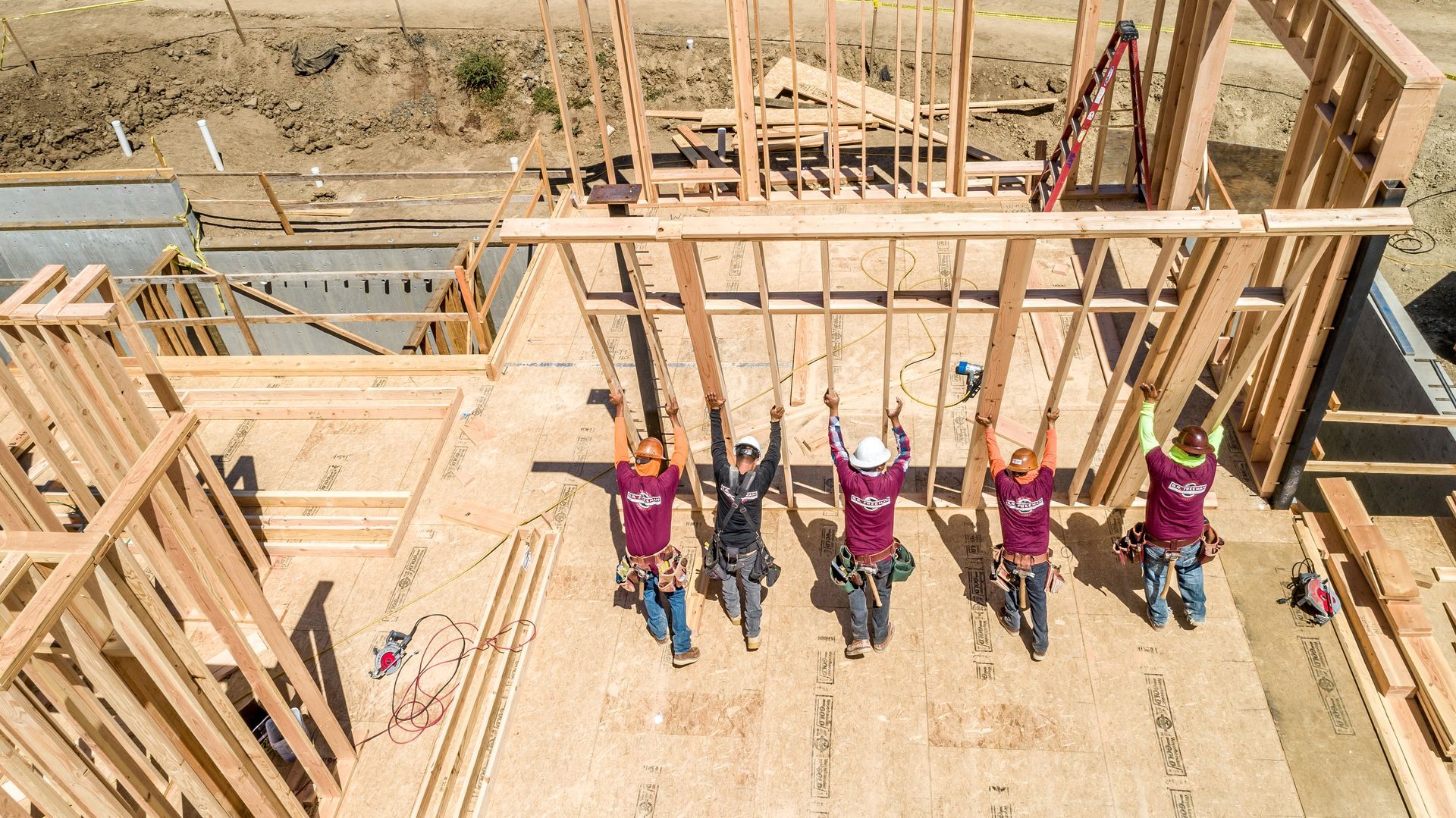 Construction workers lifting wooden beams at a building site, viewed from above