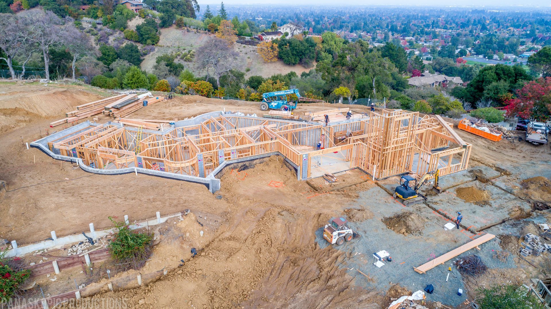 Aerial view of a house foundation under construction on a hillside, surrounded by dirt and trees.