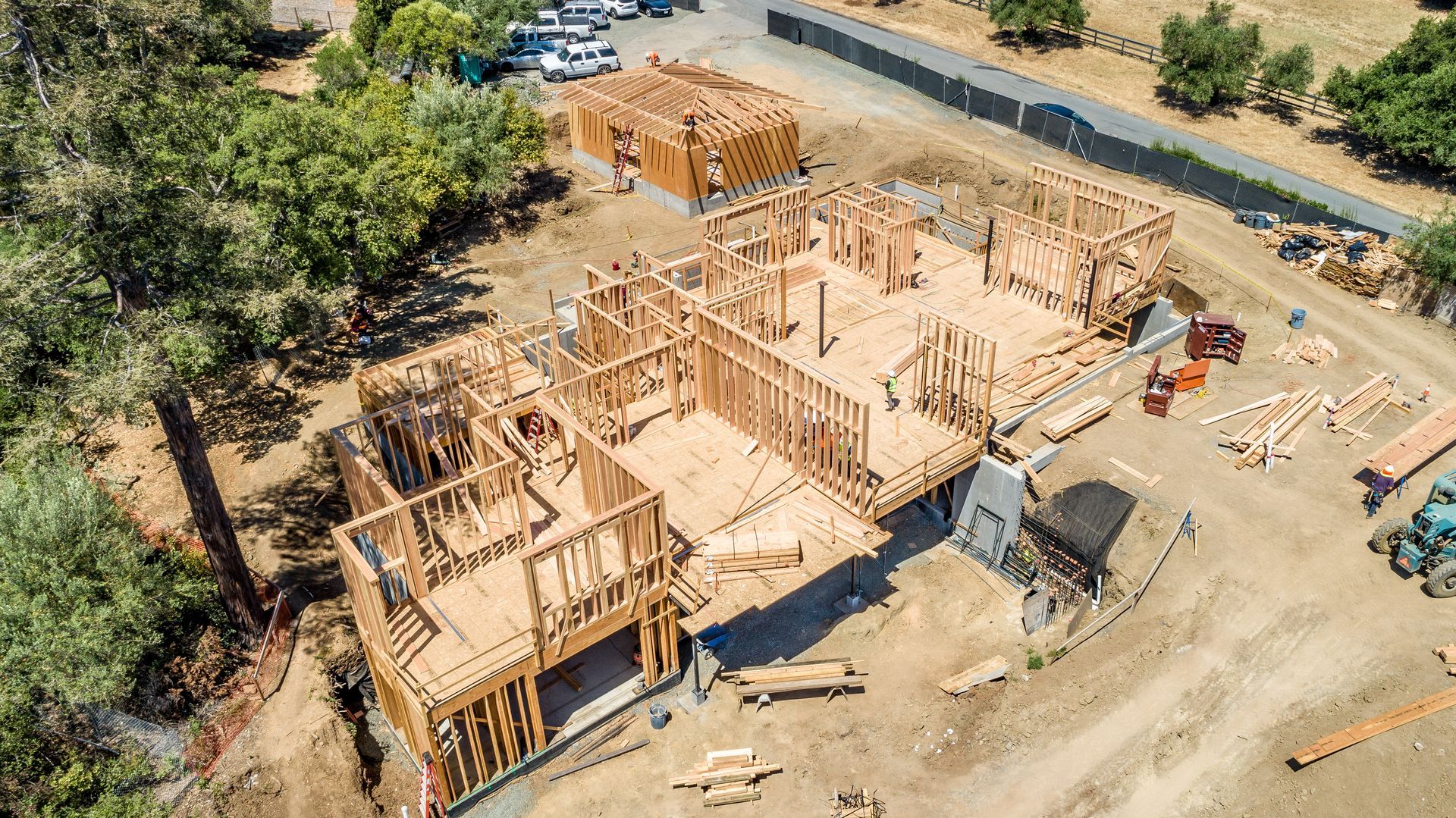 Aerial view of a wood-framed house under construction on a dirt lot with trees nearby