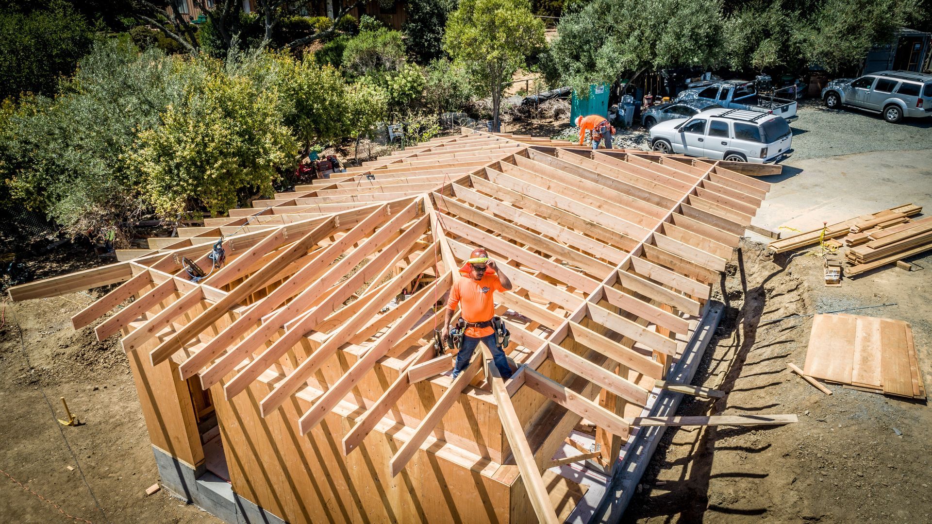Construction workers framing a wooden house roof at a building site with tools and lumber nearby
