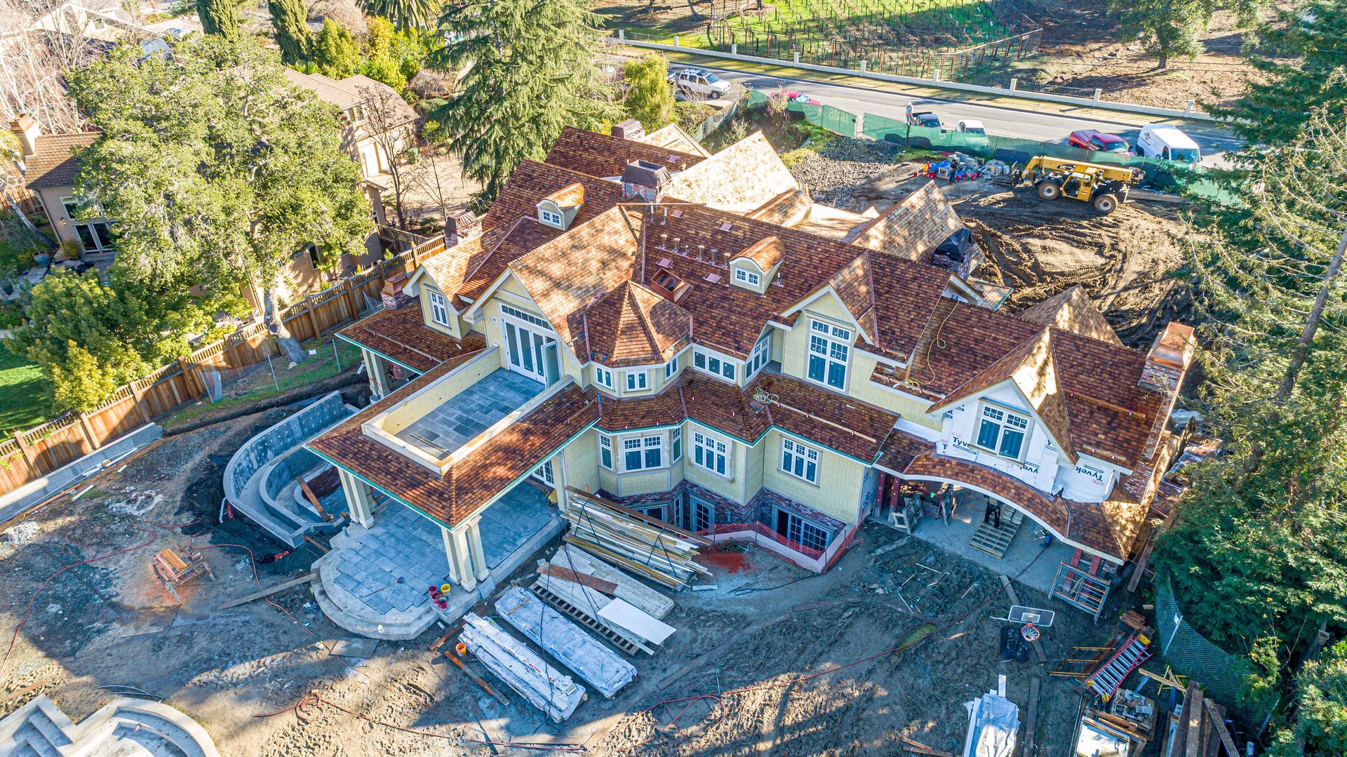 Aerial view of a large Tudor-style mansion with a stone patio, surrounded by trees and landscaping.