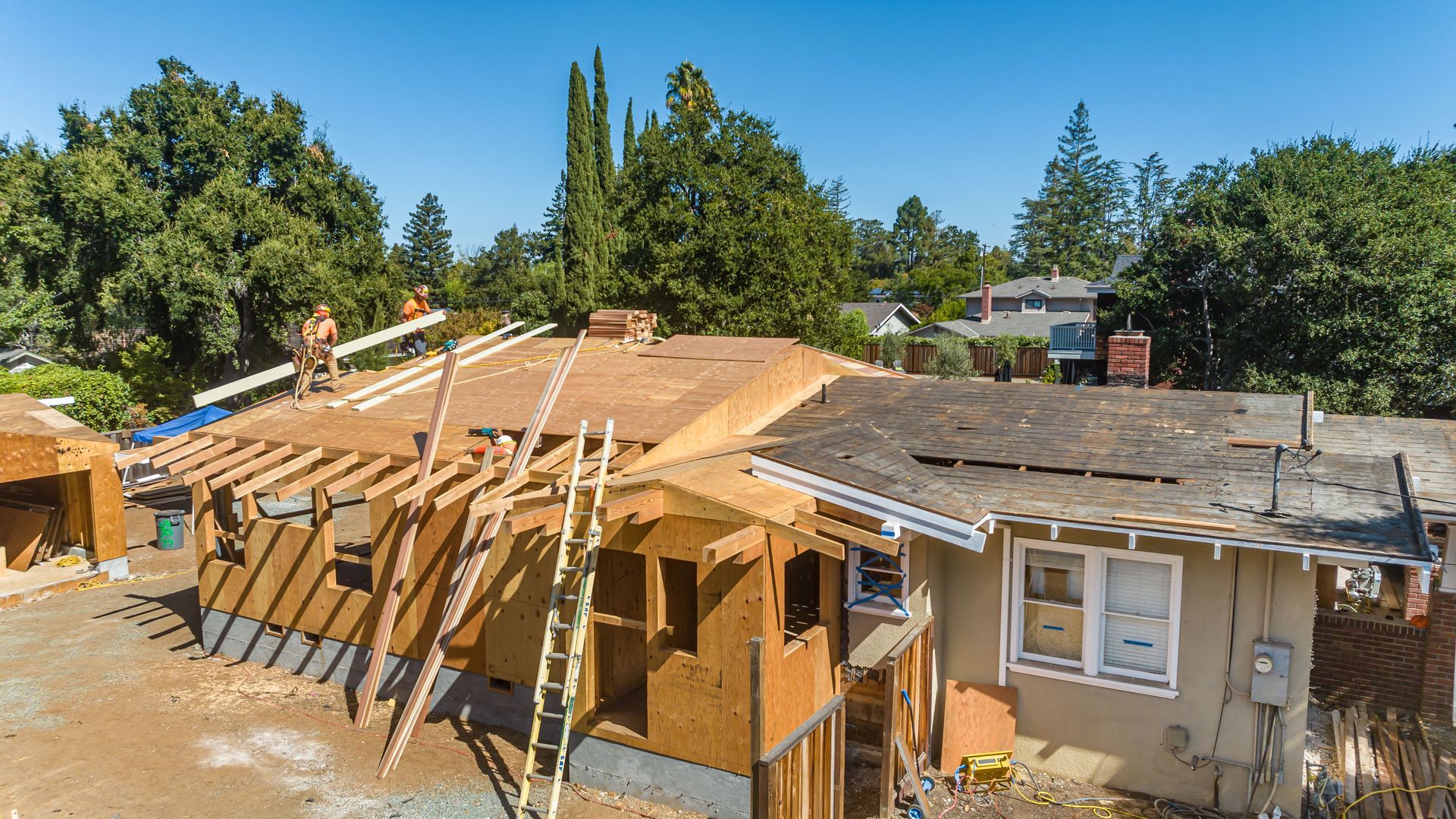 Collapsed roof on a damaged house with exposed wooden beams and surrounding debris under a clear blue sky