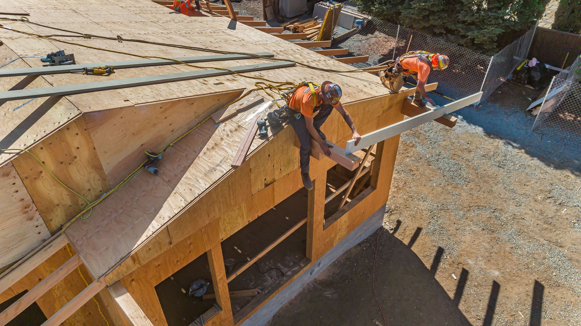 Construction workers on a roof framing a house, with lumber and tools visible.