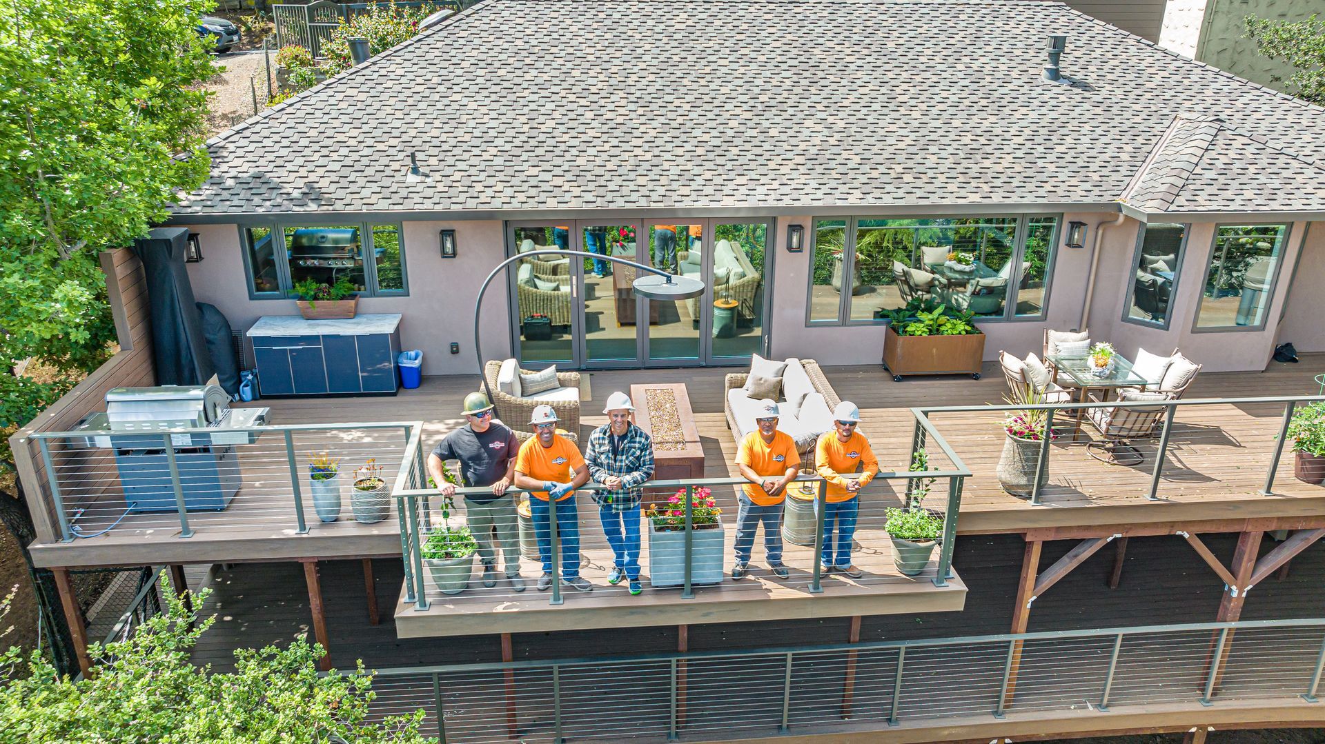 People posing on a deck outside a house, with a pool and patio furniture in the background