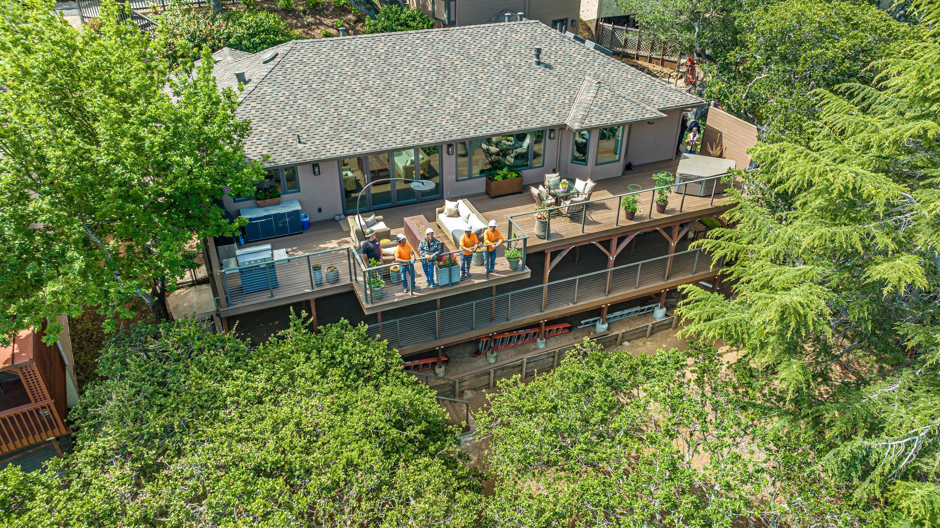 Elevated outdoor deck restaurant with tables, chairs, and umbrellas amid lush green trees