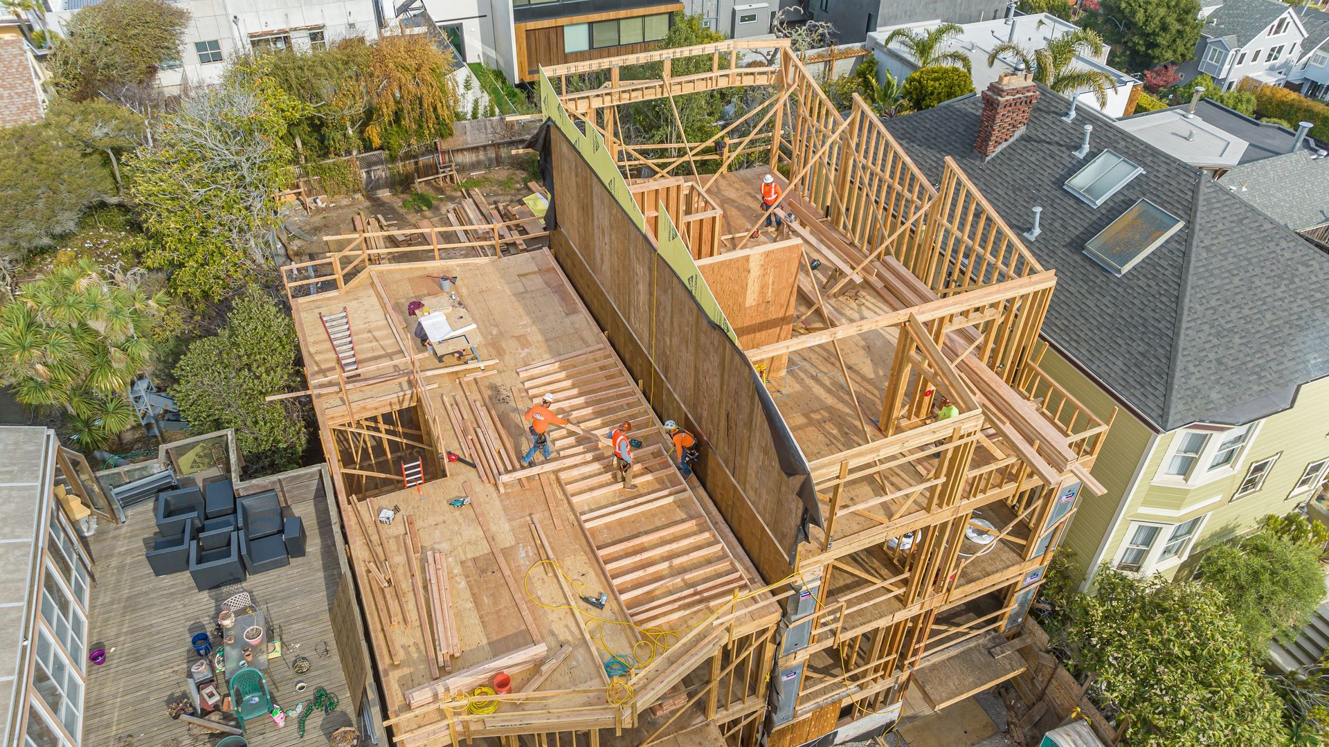 Aerial view of a house under construction with exposed wooden framing and roofing work