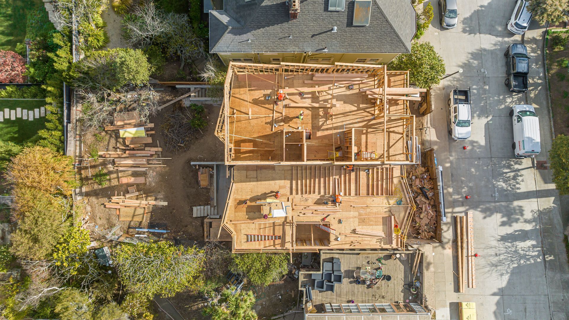 Aerial view of a house under construction with exposed wooden framing beside a street and trees