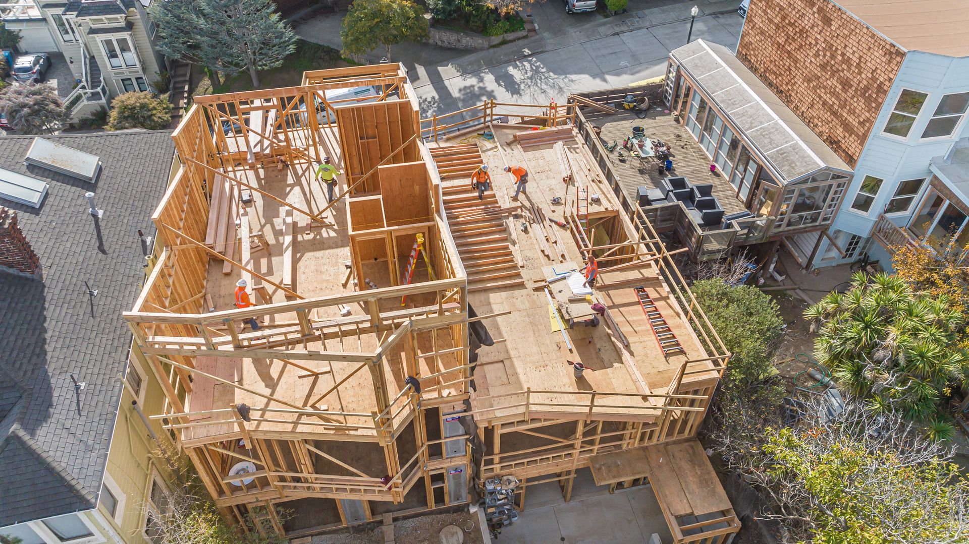 Aerial view of a house under construction with wooden framing and scaffolding in a residential neighborhood