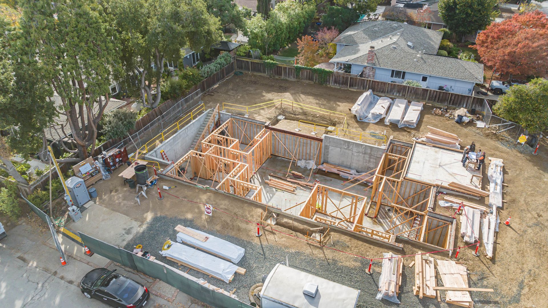 Aerial view of a building under construction with wooden framing, concrete foundation, and materials on site