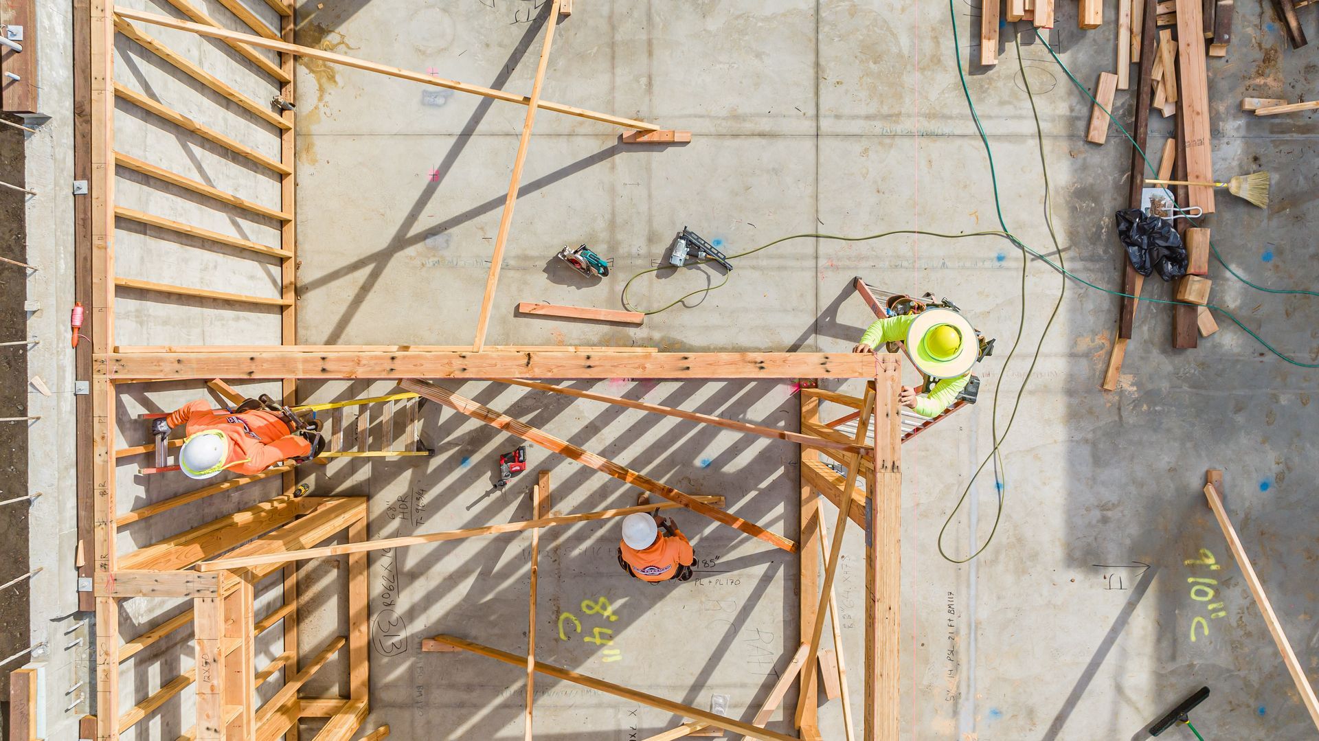 Overhead view of construction workers on a concrete site with wooden framing and safety gear