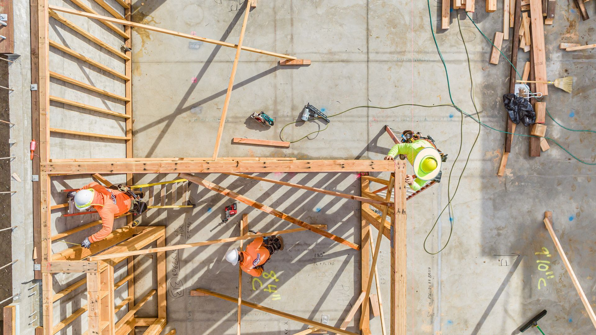Construction workers on a high-rise frame with scaffolding and concrete floor.