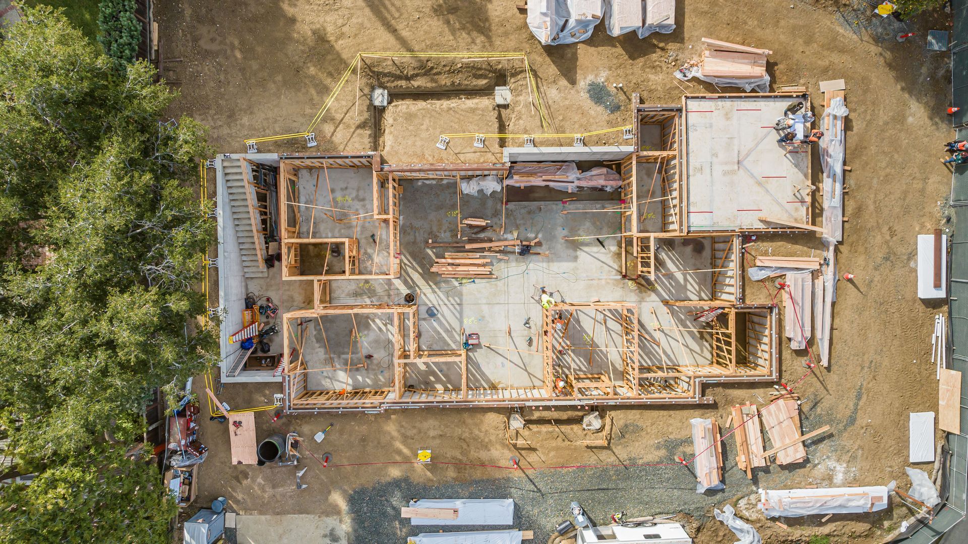 Aerial view of a house under construction with exposed wooden framing and surrounding dirt lot.