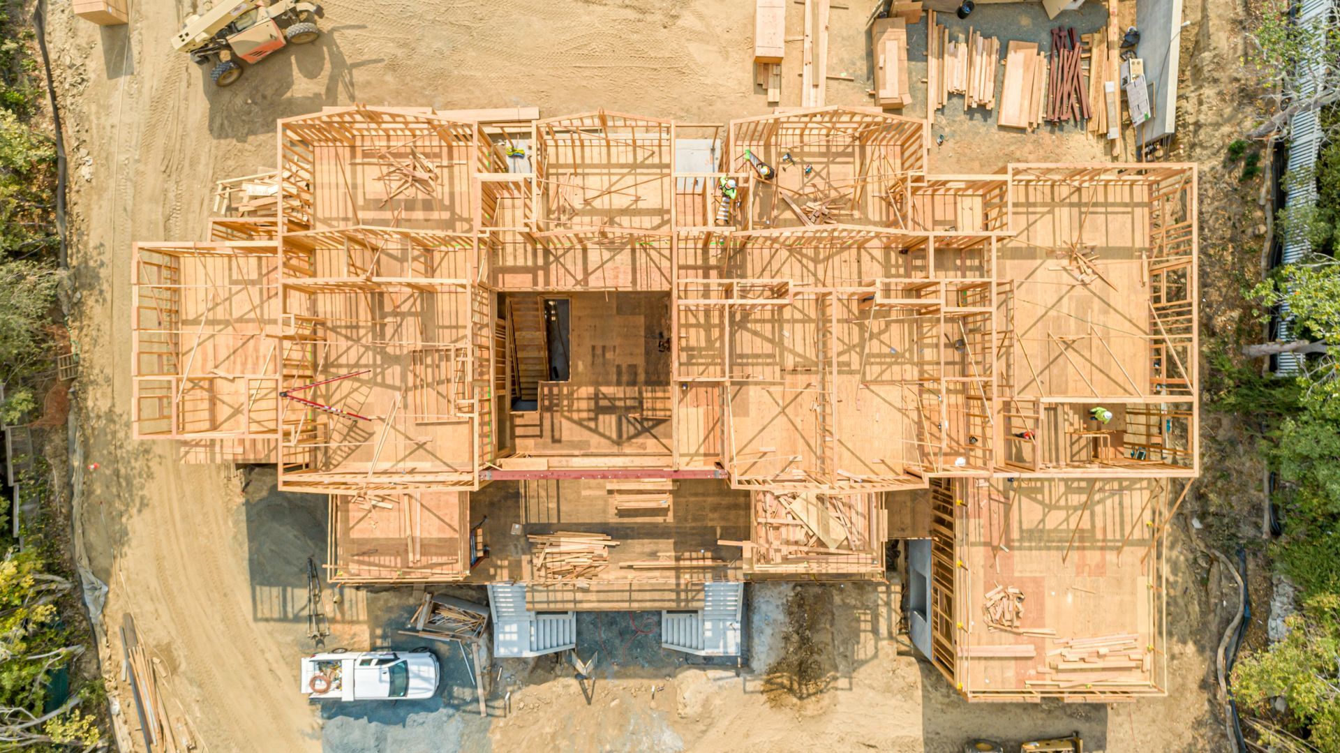 Aerial view of a house under construction with wooden framing and a parked white vehicle nearby.