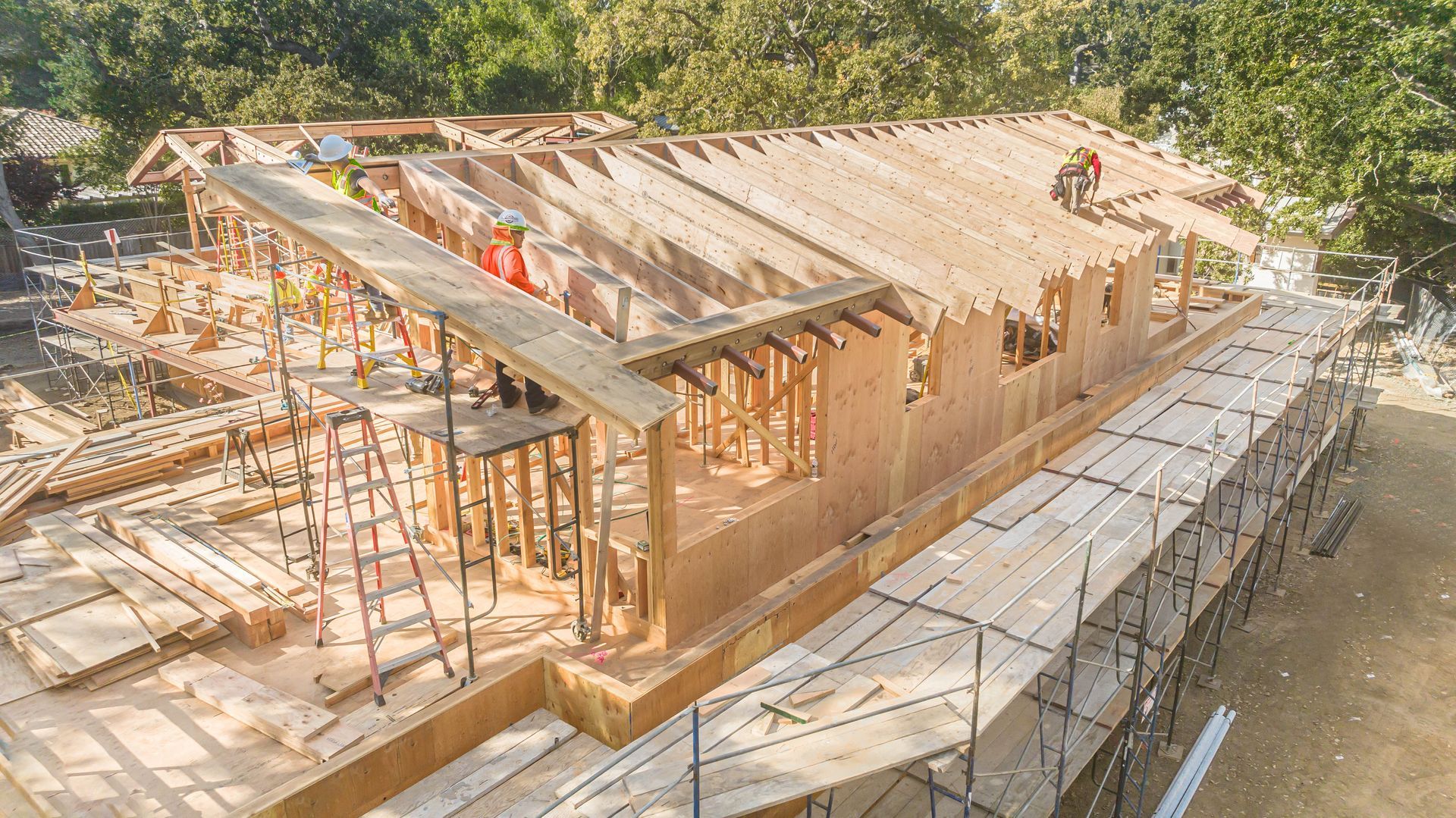Partially built wooden house with roof framing and scaffolding on a construction site