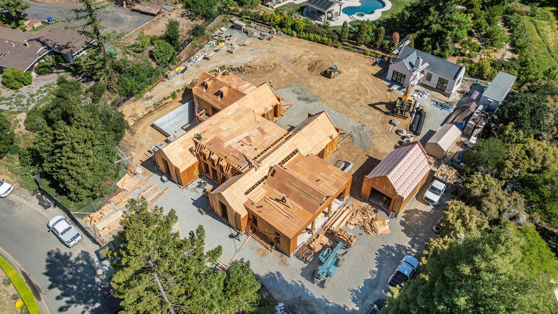 Aerial view of a partially built house with a tan roof and surrounding trees, cars, and neighboring homes.