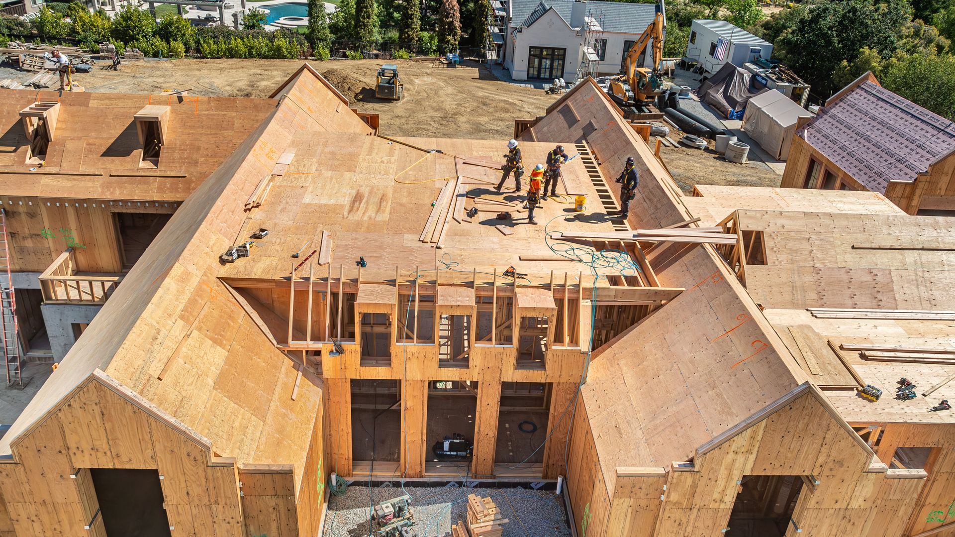 Aerial view of a house under construction with workers on the roof and exposed wooden framing.